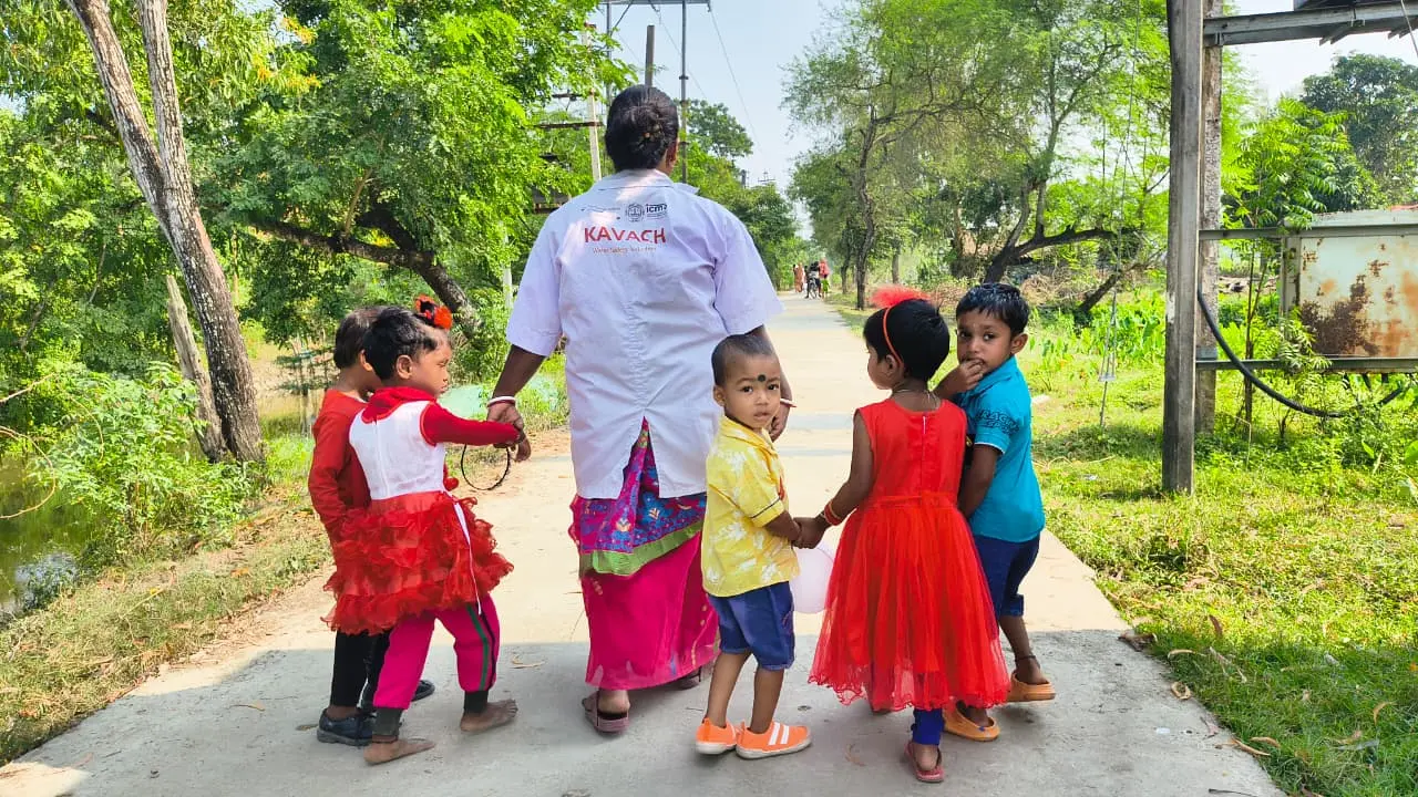 A KAVACH caregiver walking with young children along a village road
