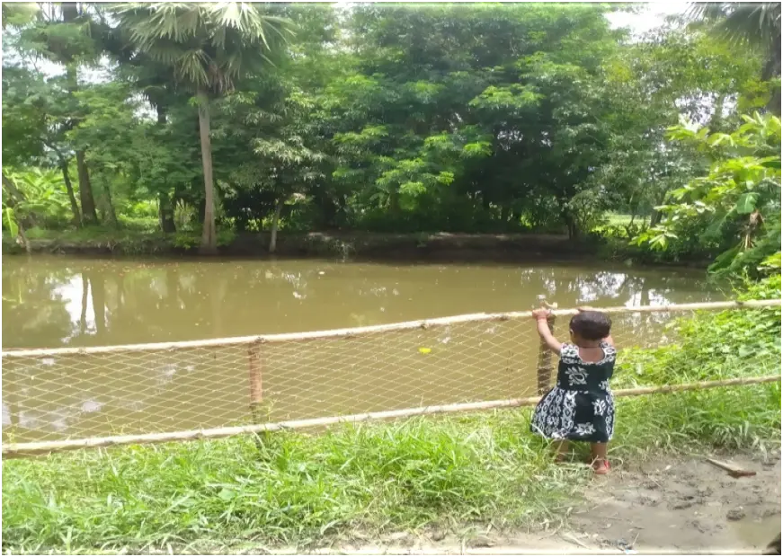 A young child standing behind locally adapted protective fencing beside a pond
