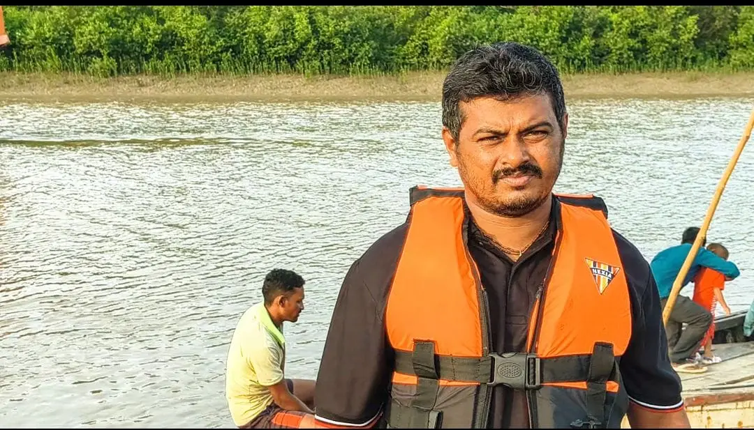 A man wearing an orange life jacket beside a waterway and boat